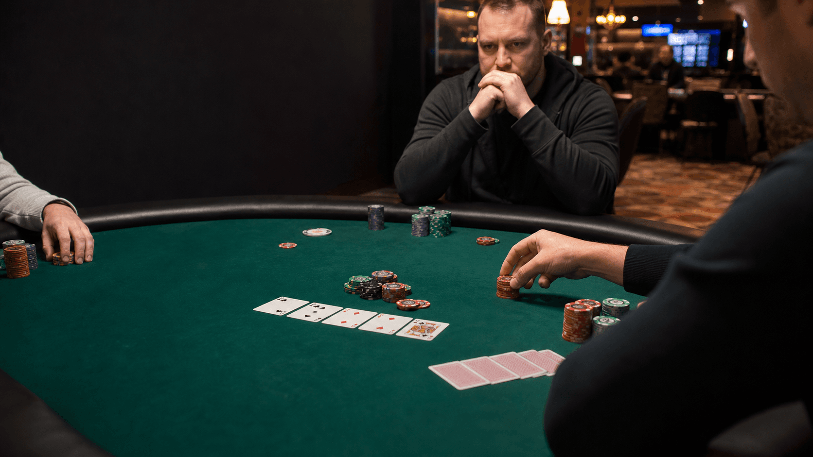 A man with clasped hands watches a small live Omaha pot from across the table.